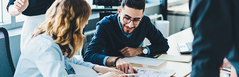 Male and female entrepreneur sitting at a table with two other team members. Reviewing a business plan outline to discuss the main components they need to cover.