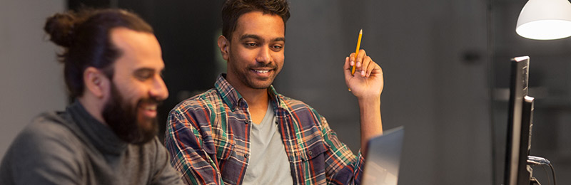 Two male entrepreneurs sitting at a desk looking at the computer, having a discussion about if they need to legally submit for a patent or other form of intellectual property.