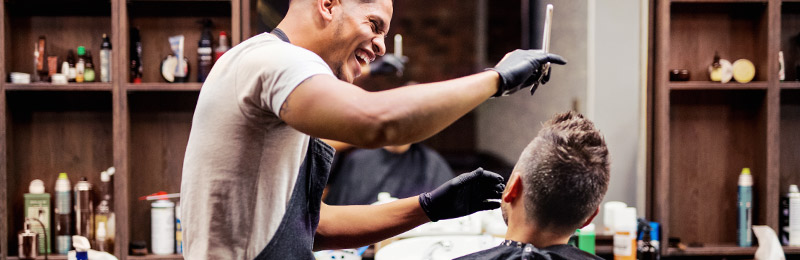 Male entrepreneur in his barber shop giving a customer a haircut. This customer is part of the entrepreneur's target market.