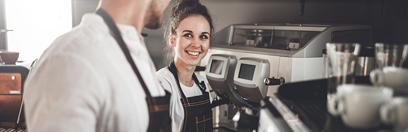 One male and one female employee standing together in front of an espresso machine. Represents people that are part of a personnel plan.