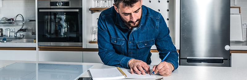 Male entrepreneur sitting in workshop at a drafting table working on documenting early orders to show business traction.