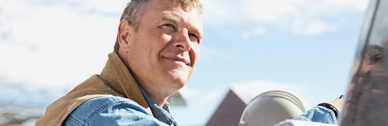 Male entrepreneur leaning up against his truck while staring out into the distance smiling. Thinking about how he'll exit his business.