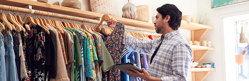 Male entrepreneur standing by a rack of clothes selecting a women's shirt to categorize.