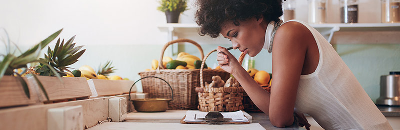 Female entrepreneur sitting at her kitchen table reviewing a sheet of key business ratios she tracks for her business.